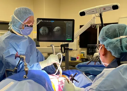 Surgical team working with tracked instruments while a navigation display shows the instrument position on the patient's imaging