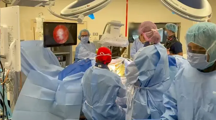 Operating theatre with the surgical team gowned around a draped patient, an endoscopic display on the left and imaging equipment behind the table