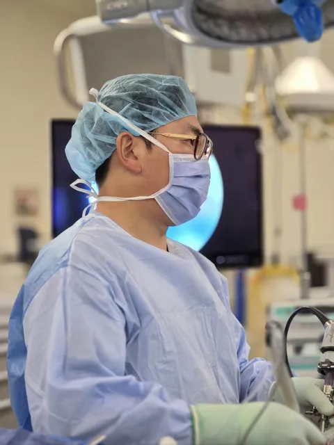 Dr. John Choi in profile at the operating table, watching the endoscopy screen during minimally invasive spine surgery