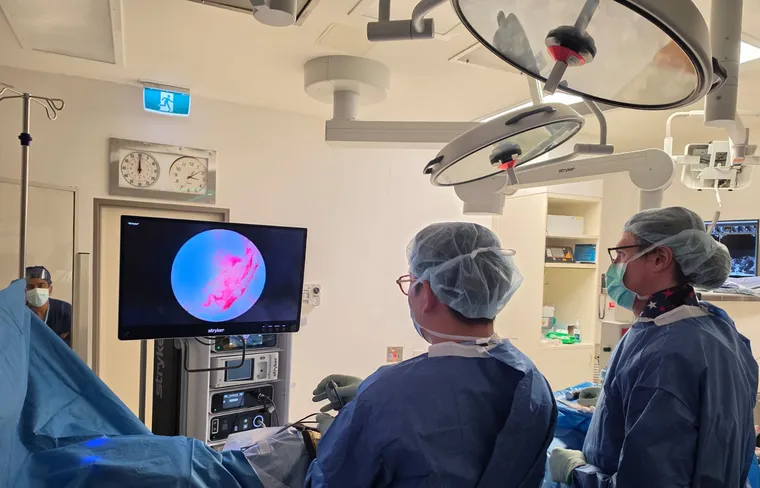 Dr. John Choi and a colleague in theatre, guided by a high-definition endoscopy screen during minimally invasive spine surgery