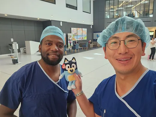 Two surgeons with a Bluey plush in a hospital lobby