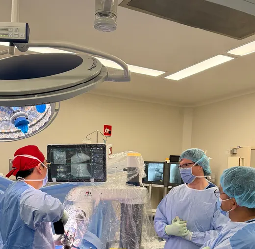 Surgical team working with the sterile-draped Globus ExcelsiusGPS robotic arm, its navigation screen showing planned implant trajectories